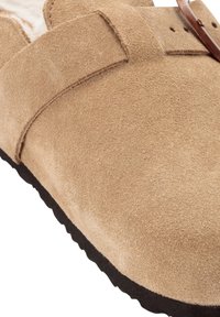 Wildleder-Slipper in Beige mit strukturierter Oberfläche, ausgestattet mit einem braunen Lederriemen und einer schwarzen Gummisohle. Weiches und komfortables Design.