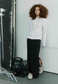 Hvid skjorte med diskret mønster, parret med en lang sort nederdel med en lændeslids. Grå sneakers fuldender looket.