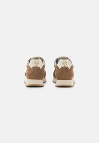 Brown suede sneakers with a beige sole. Features a gray fabric lining and logo accents on the back. Rounded shape and textured surface.