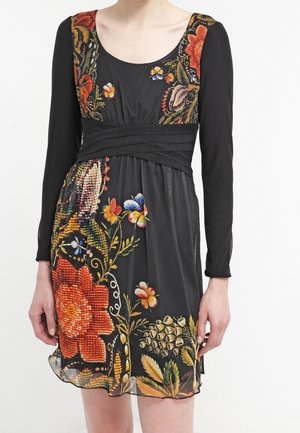 Musta pitkähihaen mekko, jossa leveä vyötärönauha ja värikäs kukka- ja perhospistely edessä ja hihoissa.