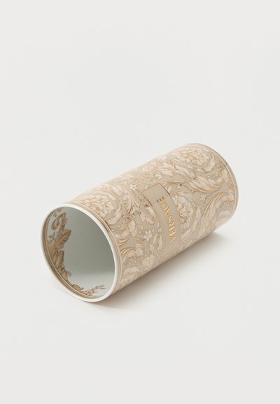 Contenant cylindrique beige avec des motifs floraux et feuillus complexes, présentant une étiquette centrale avec « VERSACE » en relief doré.