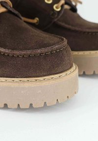 Scarpe in suede marrone con punta rotonda, suola in gomma color tan con un motivo frastagliato, lacci in pelle e occhielli in tono oro.
