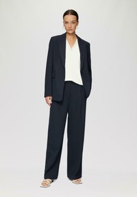 Marine suit, samengesteld uit een blazer met één knoop, wijde broek en een witte V-hals top. Kenmerkt zich door een minimalistisch ontwerp en een soepele textuur.