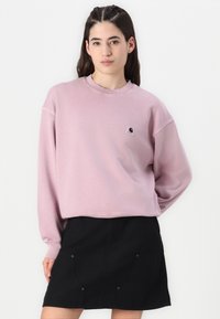 Ljusrosa sweatshirt med rund hals och långa ärmar, med en liten svart logotyp på bröstet. Sammanställd med en svart kjol.