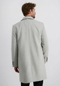 Lichtgrijze wollen overjas met een notch-kraag, lange mouwen en twee knopen op de manchetten. Heeft subtiele stikdetails en een rechte snit.