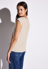 Beige kortärmad topp med rund halsringning, matchad med mörkblå jeans. Slät textur, avslappnad passform och minimalistisk design.