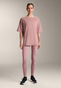 Loose-fitting, short-sleeve pink t-shirt paired with form-fitting pink leggings and black athletic shoes, set against a neutral backdrop.