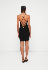 Rochie tricotată neagră cu o siluetă ajustată, având un design cu spate încrucișat și detalii cu șnur ajustabil. Se terminate deasupra genunchiului.