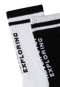 Calcetines a rayas en blanco y negro con textura acanalada. El calcetín blanco presenta la palabra "EXPLORANDO" en negro, y viceversa.