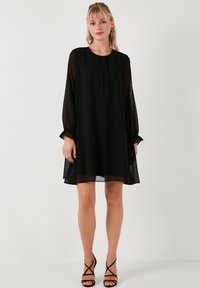 Black dress with a loose fit, long sheer sleeves, and soft, lightweight fabric. Features a round neckline and pleated detailing.