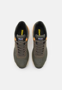 Tmavě olivově zelené tenisky s oranžovými akcenty, síťovanými panely a polstrovaným límcem. Mají texturovaný povrch a tónové tkaničky.