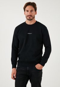 Fekete, pamut keverékből készült, kerek nyakú pulóver, ribbelt mandzsettákkal és alsó szegéllyel, fehér hímzett logóval a mellkason.