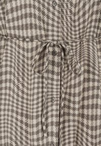 Brown and beige patterned dress with a houndstooth design, featuring buttons down the front and a tied waist for adjustment.