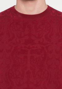 Punane kootud kampsun tekstuurse mustriga, millel on soonikuga ümara kaelusega ja pehme kangas, lähivaade detailidele.