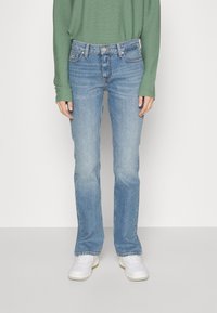 Vaqueros rectos de color azul claro con un ligero desgaste, diseño de cinco bolsillos, trabillas para el cinturón y cintura de altura media, combinados con zapatillas blancas.