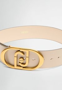 Cintura in pelle beige con una grande fibbia ovale dorata caratterizzata da un design a doppio anello. Contrassegnata da "LIU·JO" in lettere dorate.