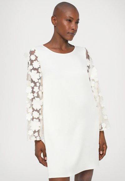 El vestido blanco presenta mangas largas y transparentes adornadas con aplicaciones florales. La tela es suave y la silueta es sencilla y ajustada.