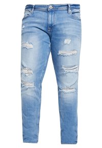 Jeans in denim blu chiaro con multiple strappi e logoramenti sul davanti, sulle cosce e sulle ginocchia, dotati di chiusura a bottoni e zip.