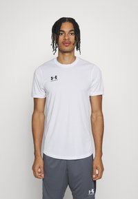 Biała sporta krekla ar īsām piedurknēm, izgatavota no elpojošas auduma. Tam ir apaļa kakla izgriezums un melns Under Armour logo uz krūtīm.