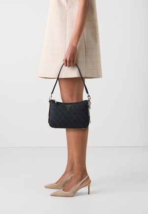 Schwarze Lederhandtasche mit geprägtem Logo, Reißverschluss und abnehmbarem Schulterriemen. Glatte Textur und kleine Größe, gehalten von einer Person.