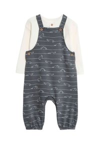 Graue Baumwoll-Latzhose mit weißen Tier- und Sonnenmustern; verfügt über Knopfträger und elastische Bündchen; kombiniert mit einem cremefarbenen Langarmshirt.