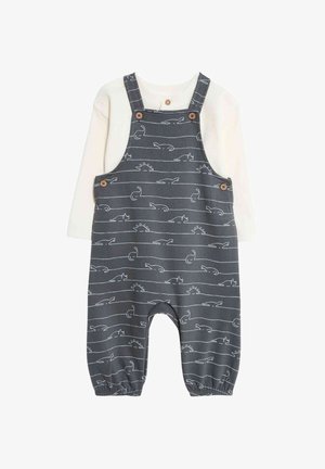 Salopette en coton gris avec des motifs d'animaux et de soleil blancs ; dotée de bretelles à bouton et de poignets élastiques ; superposée avec un haut à manches longues crème.