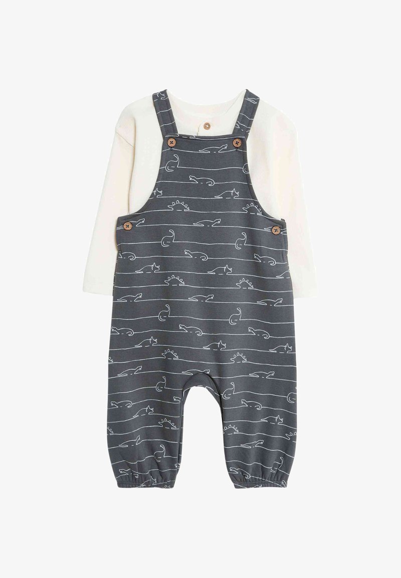 Graue Baumwoll-Latzhose mit weißen Tier- und Sonnenmustern; verfügt über Knopfträger und elastische Bündchen; kombiniert mit einem cremefarbenen Langarmshirt.