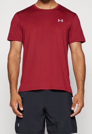 Mann trägt burgunderrotes, kurzärmeliges Sportshirt und schwarze Shorts, beide mit sichtbaren Under Armour-Logos auf Brust und Oberschenkel.