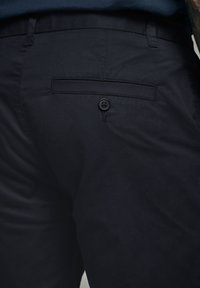 Tmavě modré kalhoty s hladkým povrchem, s jednou zadní kapsou a jednobarevným černým knoflíkem. Přizpůsobený střih s jemnými akcenty šití.