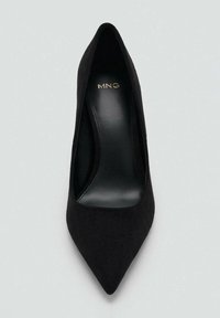 Zapato de salón de tacón alto en ante negro con punta puntiaguda, interior de cuero liso y logo dorado en la plantilla. Diseño sencillo y elegante.