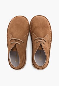 Scarpe in suede marrone con punta arrotondata, design con lacci sottili e cuciture a contrasto lungo la suola. Esterno leggero e strutturato.
