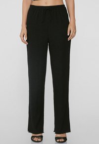Pantalons larges noirs en tissu texturé avec une taille à cordon. Présente une coupe décontractée et unourlet effiloché au niveau des chevilles.