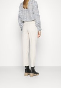 Helle, schmal zulaufende Hose mit glatter Textur, kombiniert mit einem gemusterten Langarmoberteil. Schwarze, hohe Stiefeletten runden das Outfit ab.