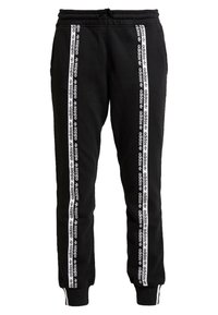 Černé tepláky vyrobené z bavlny, s bílými vertikálními pruhy a nápisem. Dole stažené, s elastickým pasem a stahovací šňůrou.