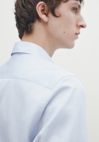 Helleblaue Hemd mit Kragen, aus einem glatten Stoff und in schmaler Passform. Verfügt über ein strukturiertes Schulterdesign und minimalistische Details.