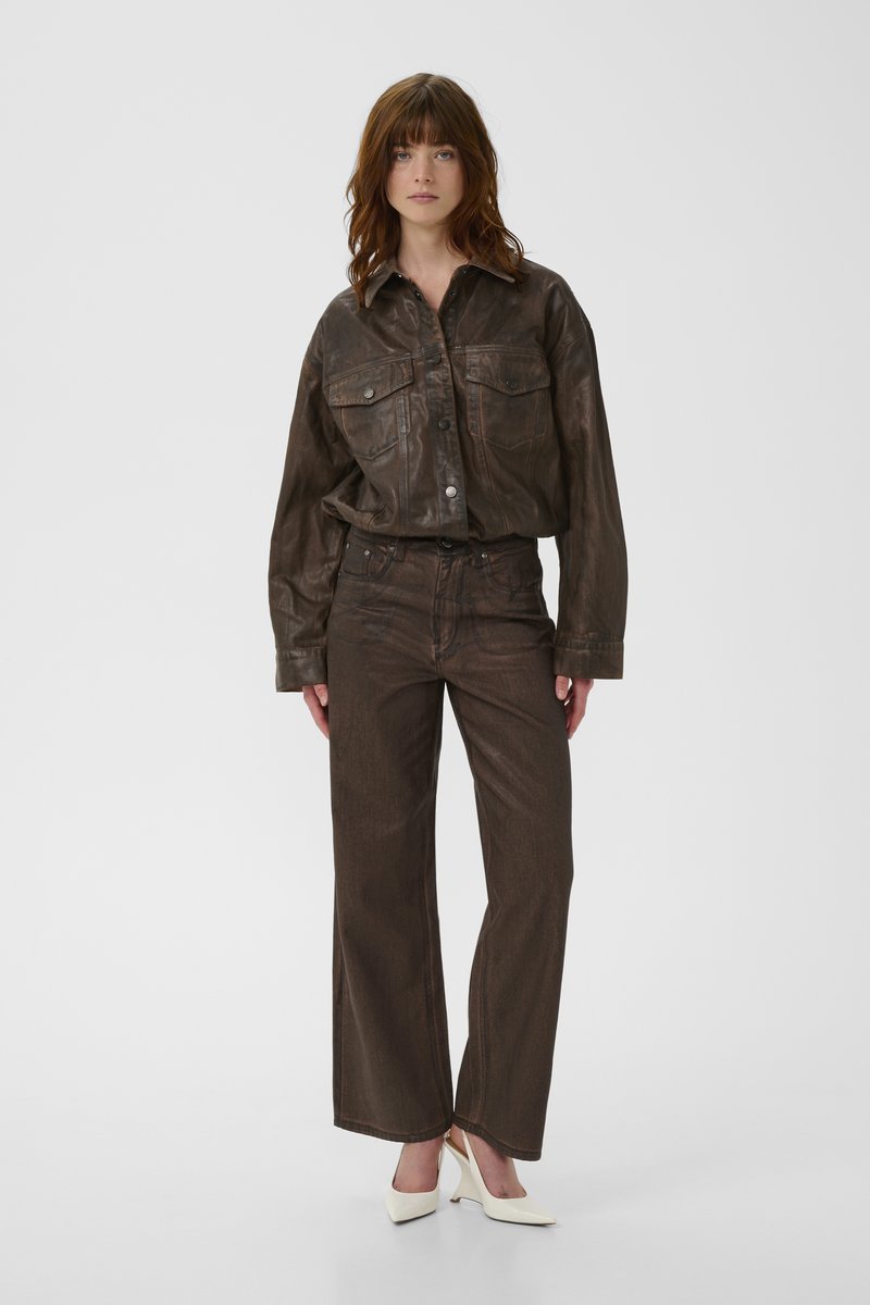 Brown leather shirt layered over matching brown pants, featuring a relaxed fit, pockets, and white heeled shoes for contrast.