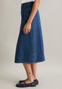 Jupe midi en denim bleu foncé avec une silhouette droite, dotée d'une taille haute, de coutures latérales et d'un ourlet qui s'évasent légèrement en bas.