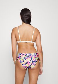 Conjunto de biquíni com um top de cor clara e parte de baixo de cintura alta com padrões abstratos multicoloridos atados nas laterais. Textura suave.