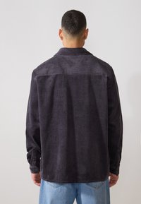 Camicia in corduroy grigio scuro con colletto, maniche lunghe, polsini con bottoni e texture a righe orizzontali sulla schiena.