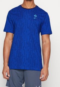 Modrý sportovní tričko s vertikálními pruhy, kulatým výstřihem, krátkými rukávy a malým logem na hrudi. Měkká tkanina se strukturovaným vzorem.