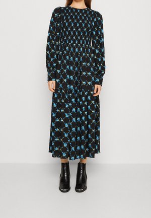 Musta pitkähihaisuus mekko, jossa on sinisen ja vihreän kukkakuosi. Mekossa on smokkayksityiskohta yläosassa ja kerroksellinen hame, yhdistetty mustiin nilkkabuutseihin.