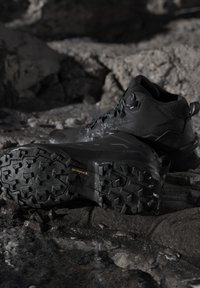 Schwarze robuste Wanderstiefel mit tiefem Profil auf felsigem, nassem Gelände, entwickelt für den Outdoor- und Trail-Einsatz.