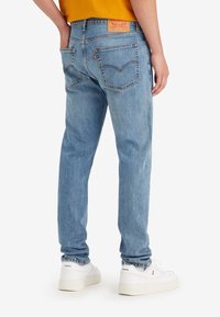 Jeans de denim azul claro con un corte recto, dos bolsillos traseros y una etiqueta de cuero con marca en la cintura. Llevados con zapatillas blancas.