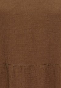 Tissu texturé marron avec une couture subtile et un détail froncé près du bord inférieur.
