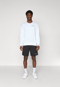 Sweat-shirt blanc avec un logo, associé à un short noir avec un logo d'accent. Des baskets blanches et des chaussettes de sport blanches complètent le look.