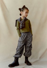 Bluză verde cu mânecă lungă asociată cu pantaloni cargo gri cu talie elastică, având buzunare laterale și botine negre. Material texturat pe toată suprafața.