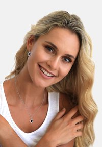 Sølv smykkesæt med en rund vedhæng halskæde og matchende øreringe med en sort cirkulær detalje. Model iført en hvid tanktop.