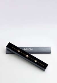 Bracelet en chaîne dorée avec des accents hexagonaux, présenté dans une boîte noire avec une finition texturée et un logo. L'intérieur noir contraste avec le bijou.