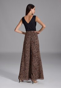 Haut sans manches noir avec un dos en V, associé à un pantalon fluide taille haute avec un imprimé léopard dans des tons de marron et de noir.