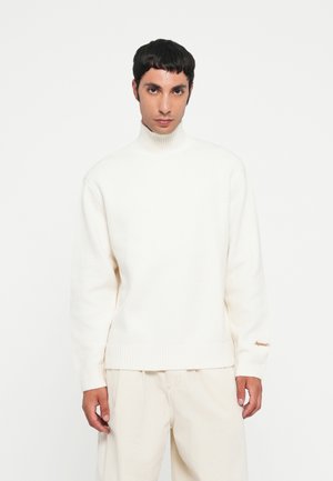 Suéter blanco de cuello alto con un acabado texturizado y puños acanalados. Presenta un sutil detalle de marca en dorado en la manga derecha.